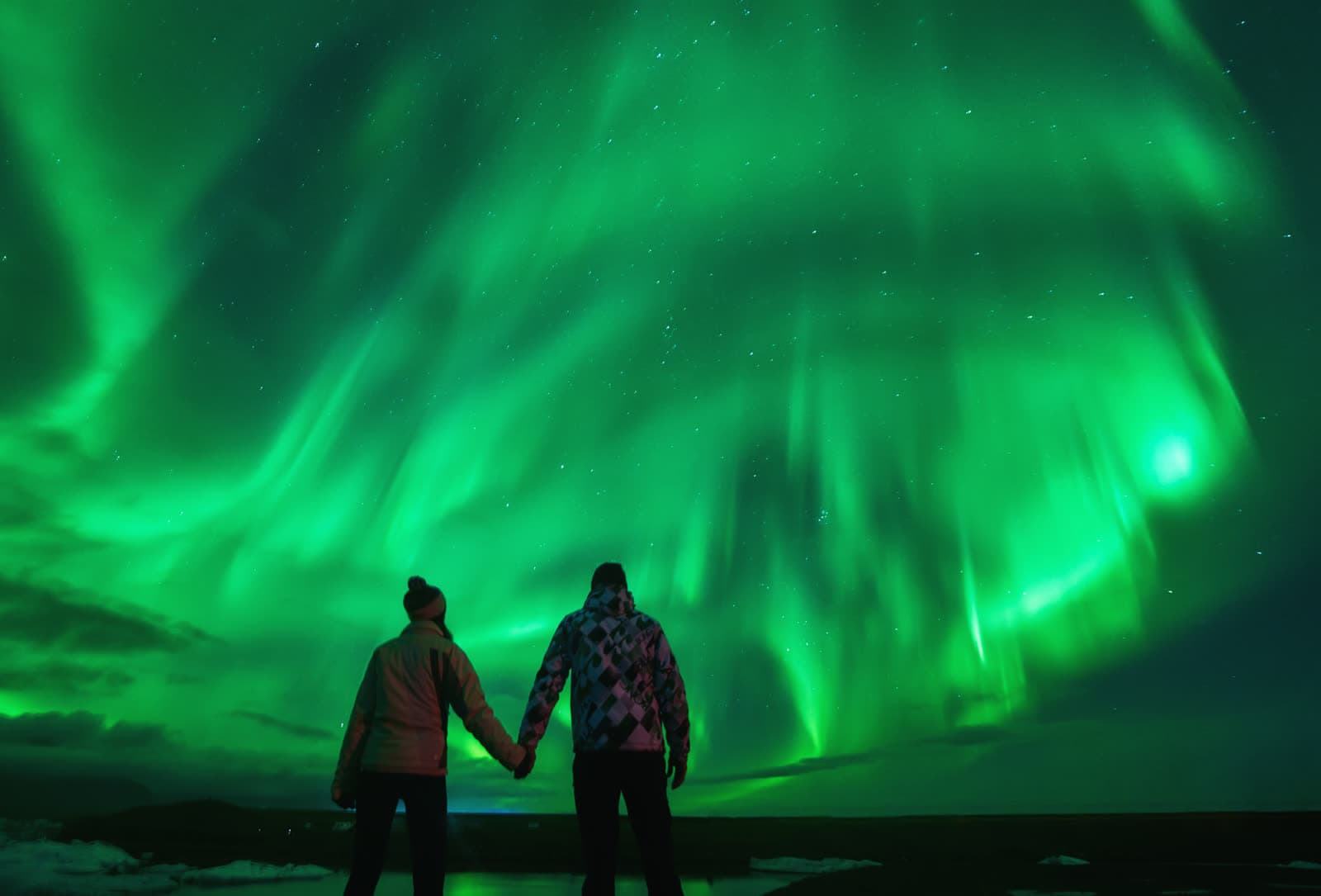 Aurora boreal sobre Jökulsárlón en otoño — pareja observando las auroras boreales en Islandia reflejadas en la laguna glaciar