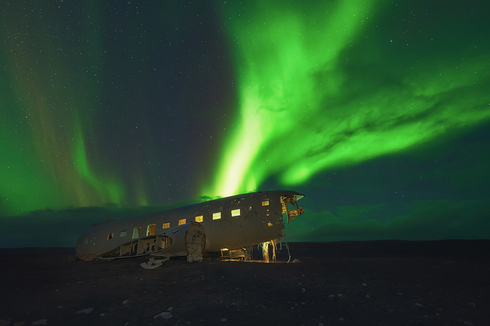 Auroras boreales sobre el avión estrellado de Islandia de noche — luz interior LED y grupo coordinado iluminando el fuselaje