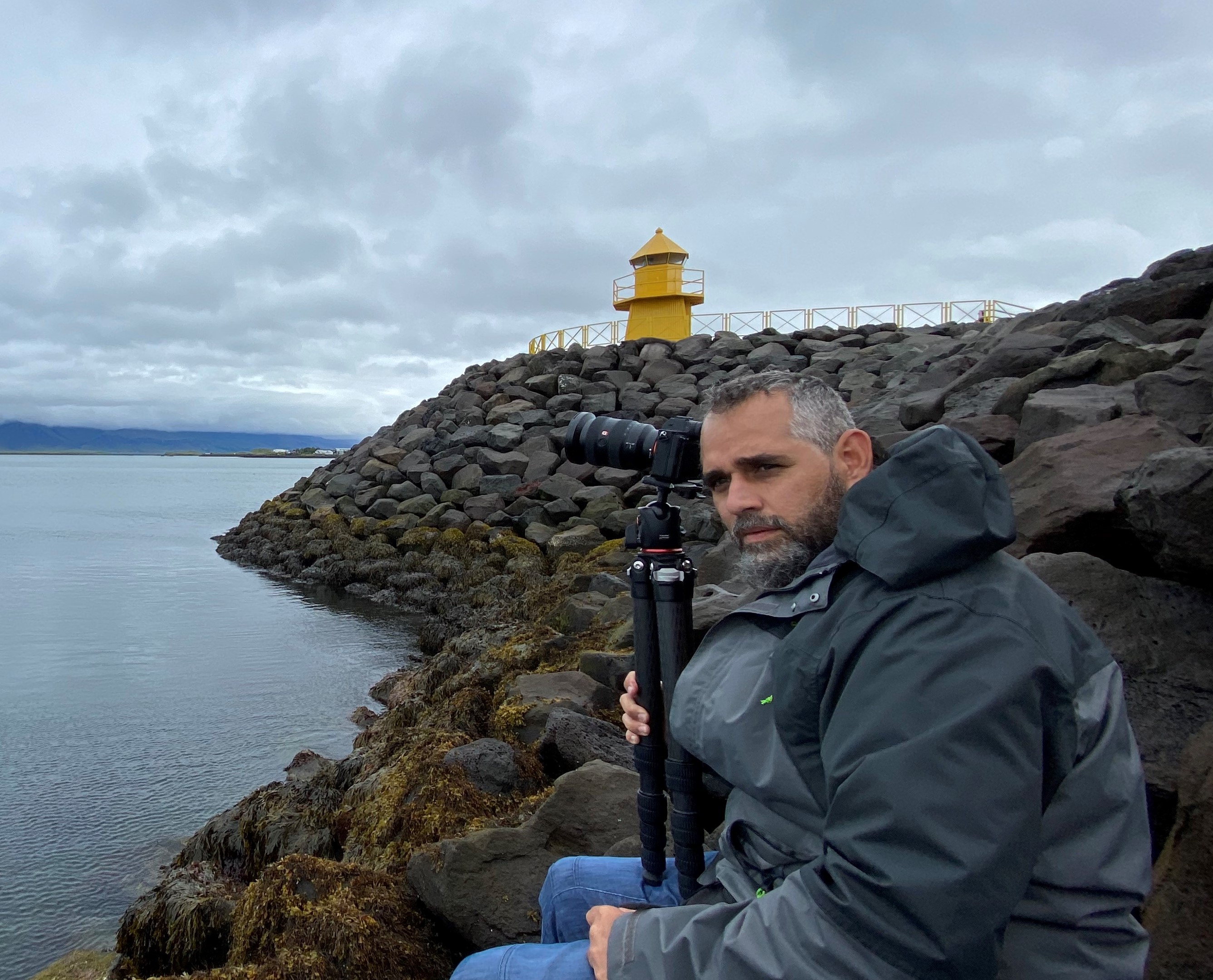 Manu con cámara en Islandia, faro al fondo — planificación personalizada de viajes