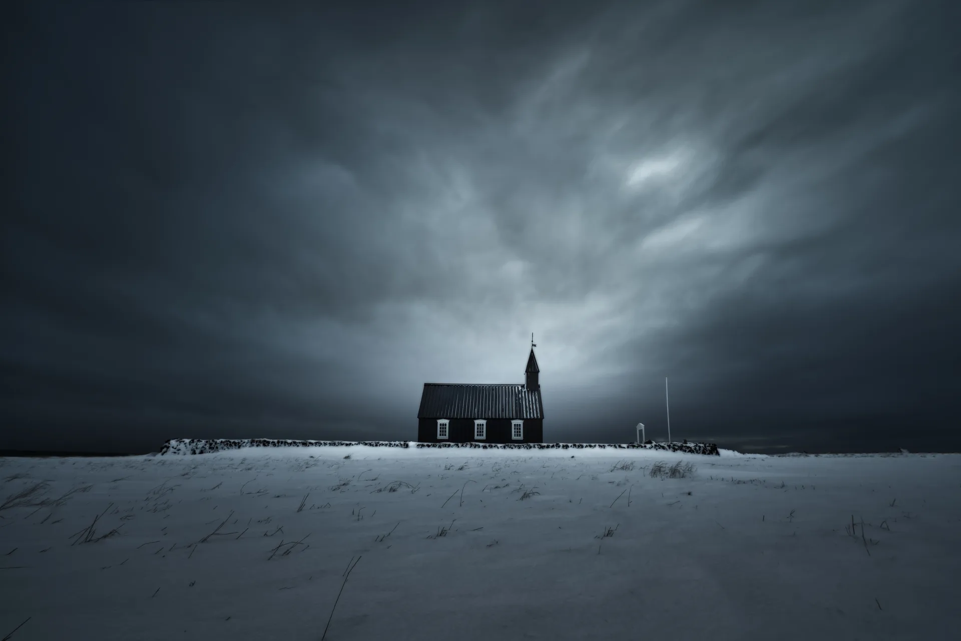 Iglesia negra de Búðir en ventisca de invierno, Snæfellsnes, Islandia — luz abriéndose sobre el tejado oscuro